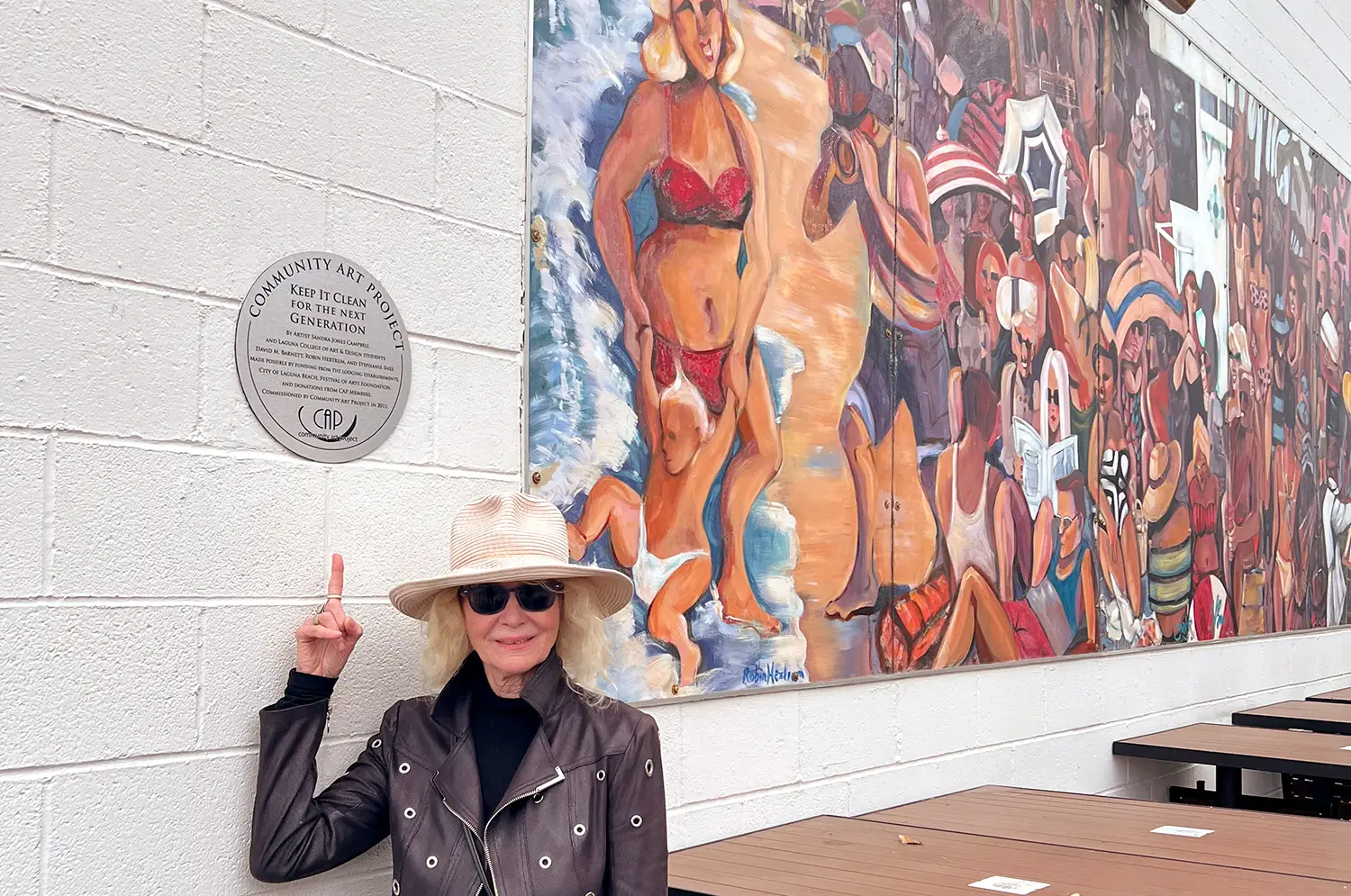 Artist Sandra Jones Campbell posing in front of a mural and a plaque.