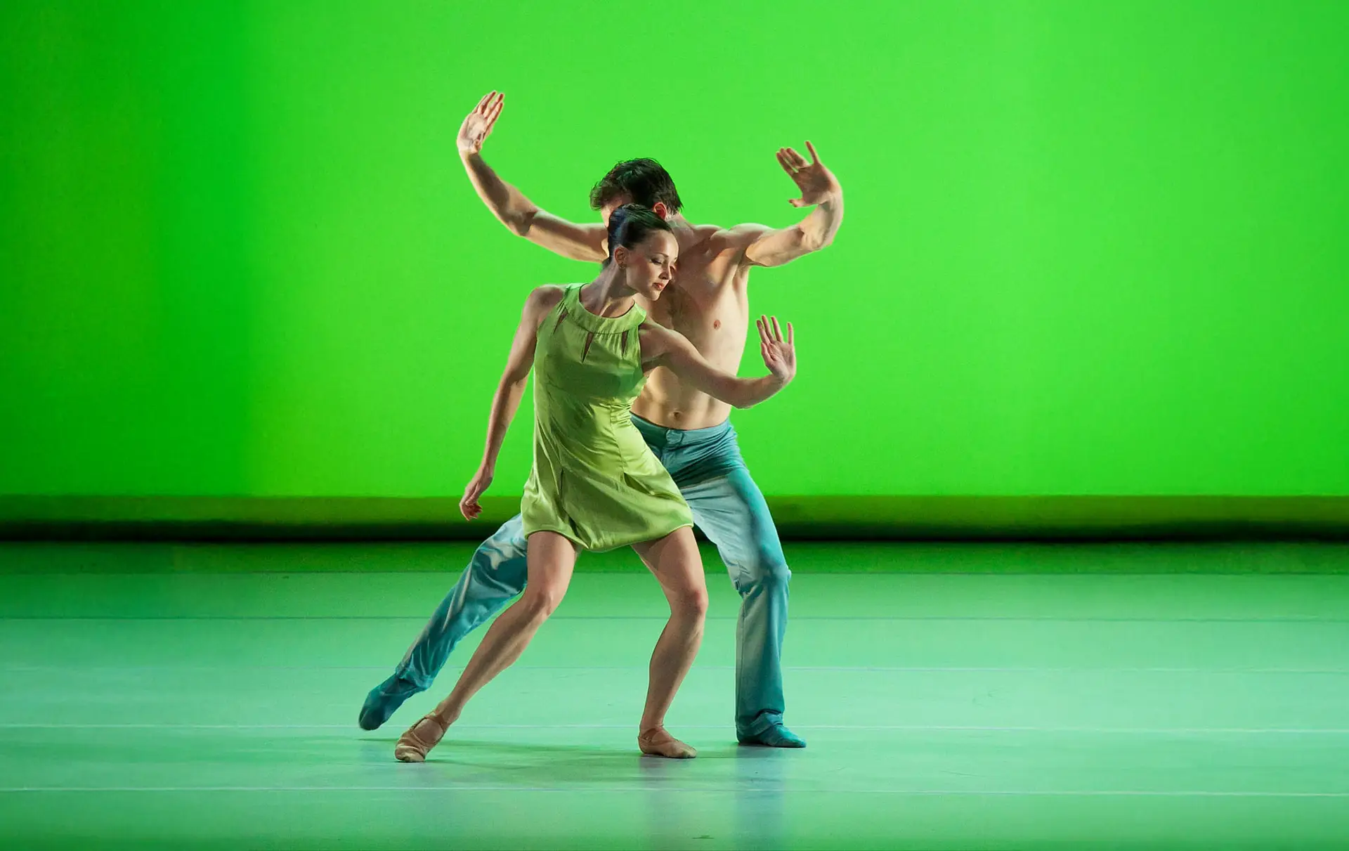 A male and female dancer striking a pose in front of a brilliant green background