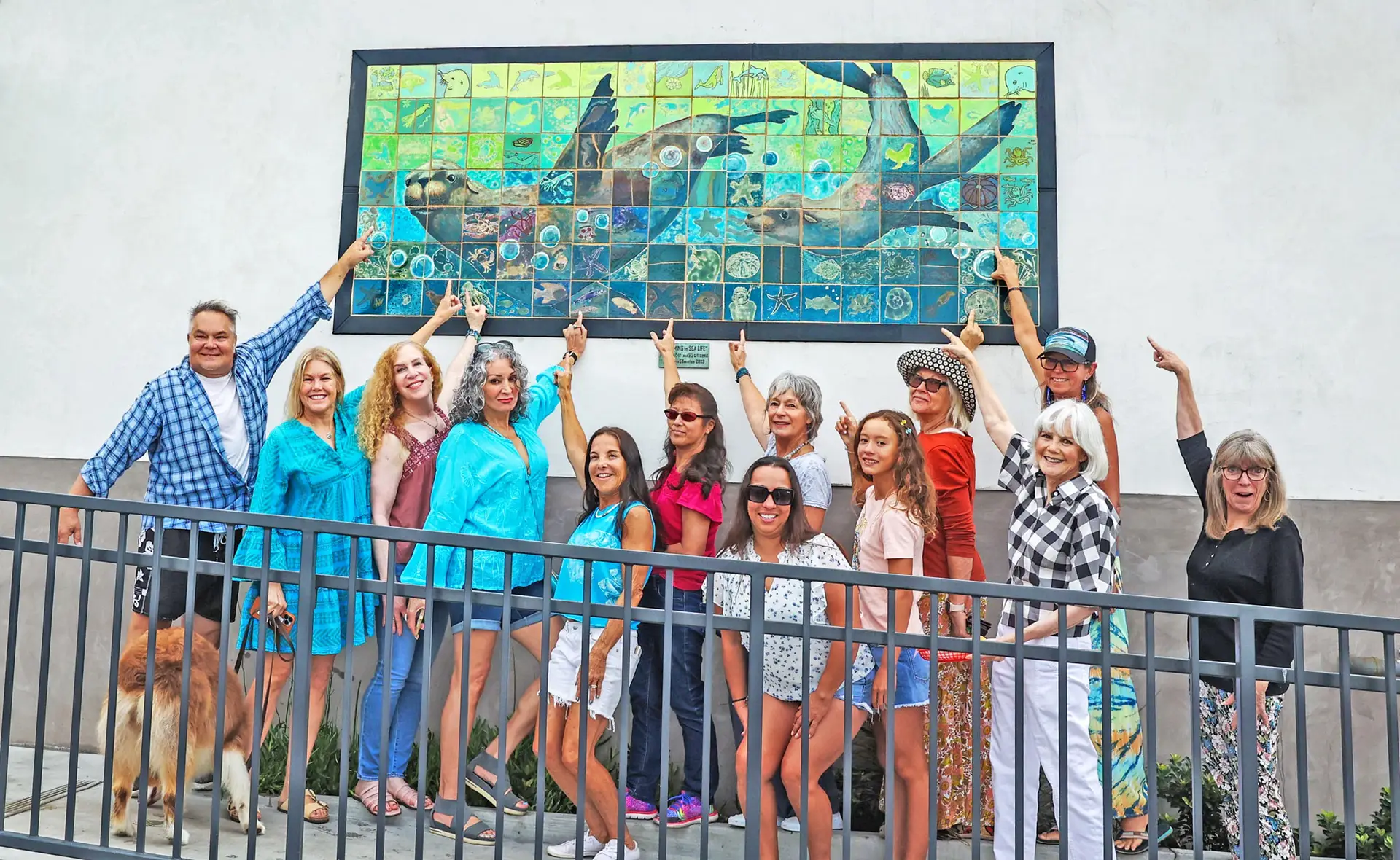 LOCA artists proudly pointing to tiles they painted on a mural of Sea Lions