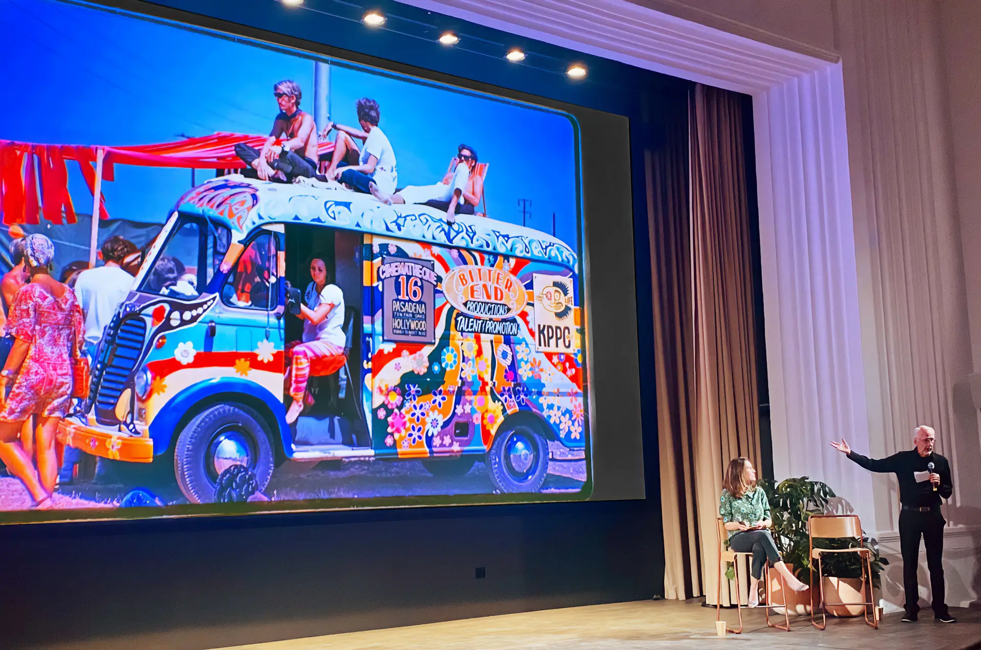 Speaker on stage commenting on an image displayed on a theater screen
