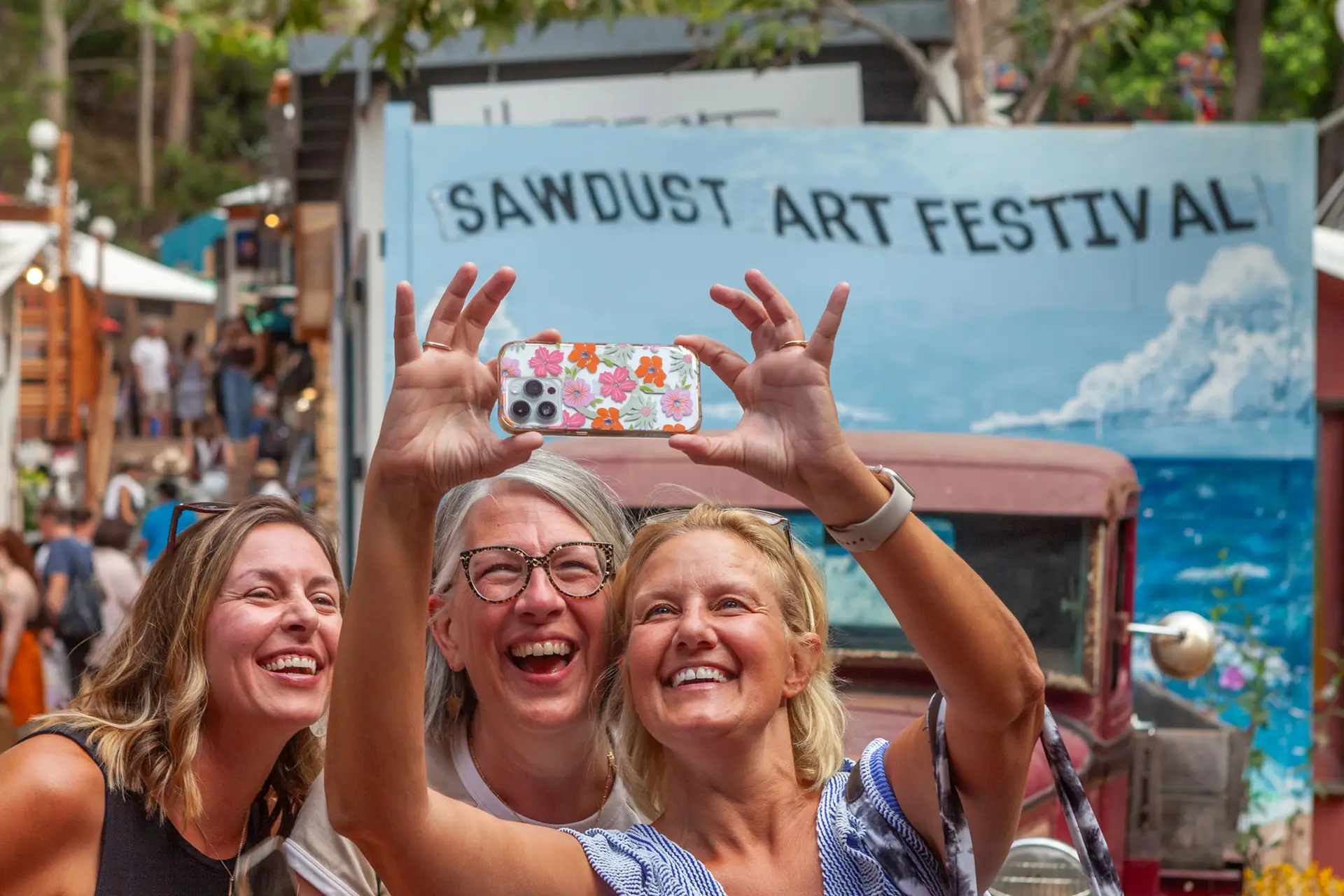 Three Female friends taking a selfie together in front of the festivals mural
